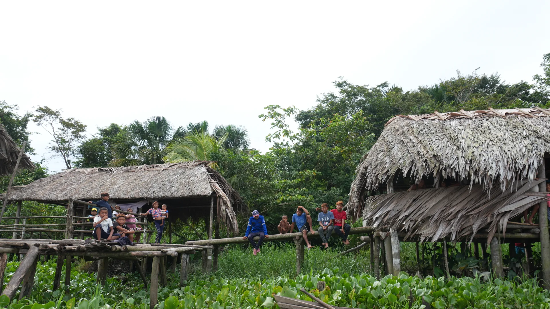 Niños y jóvenes Warao reunidos sobre las barandas de un palafito, con una canoa de madera en primer plano