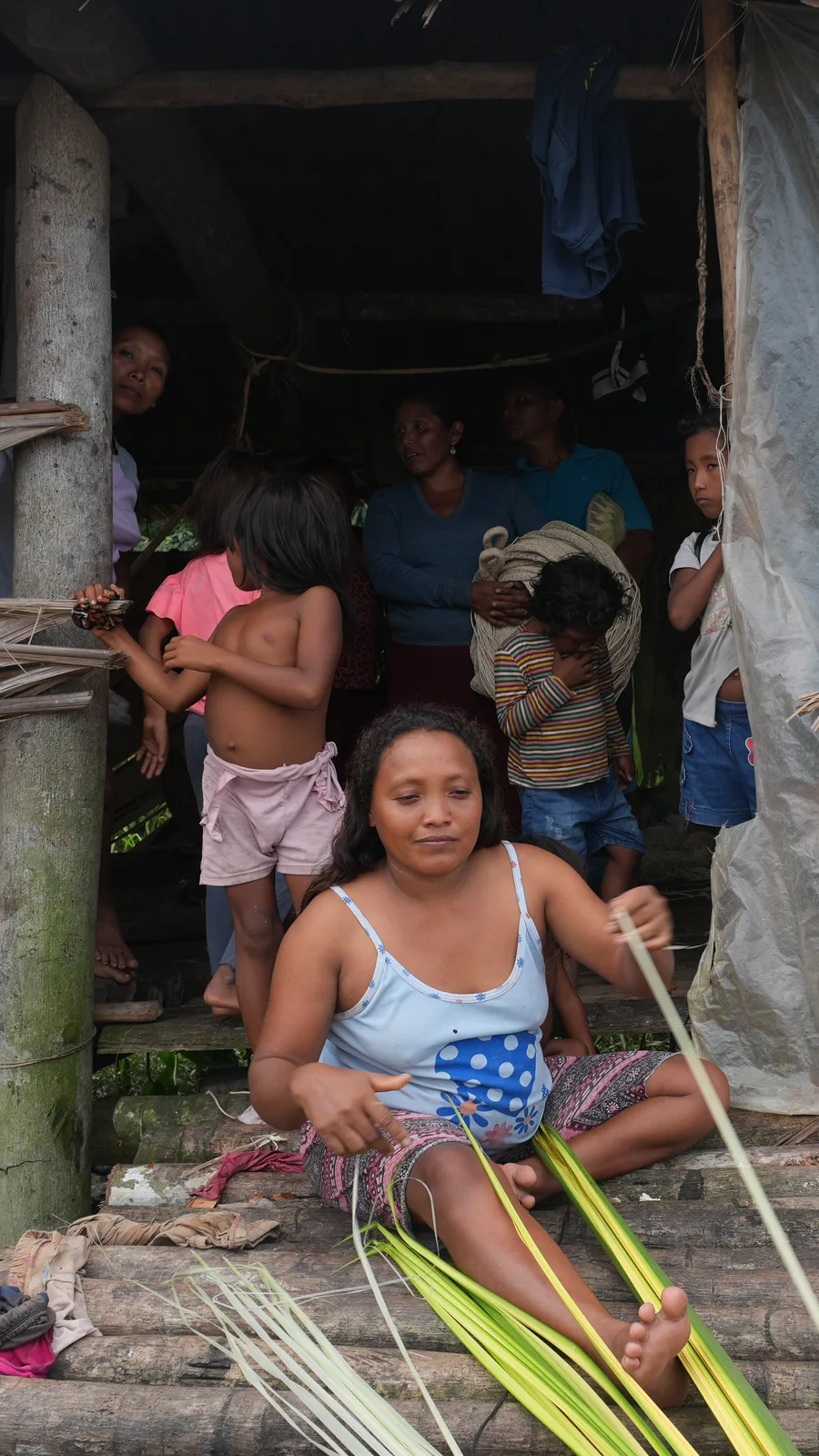 Mujer Warao tejiendo fibra de moriche rodeada de niños y familiares en su palafito